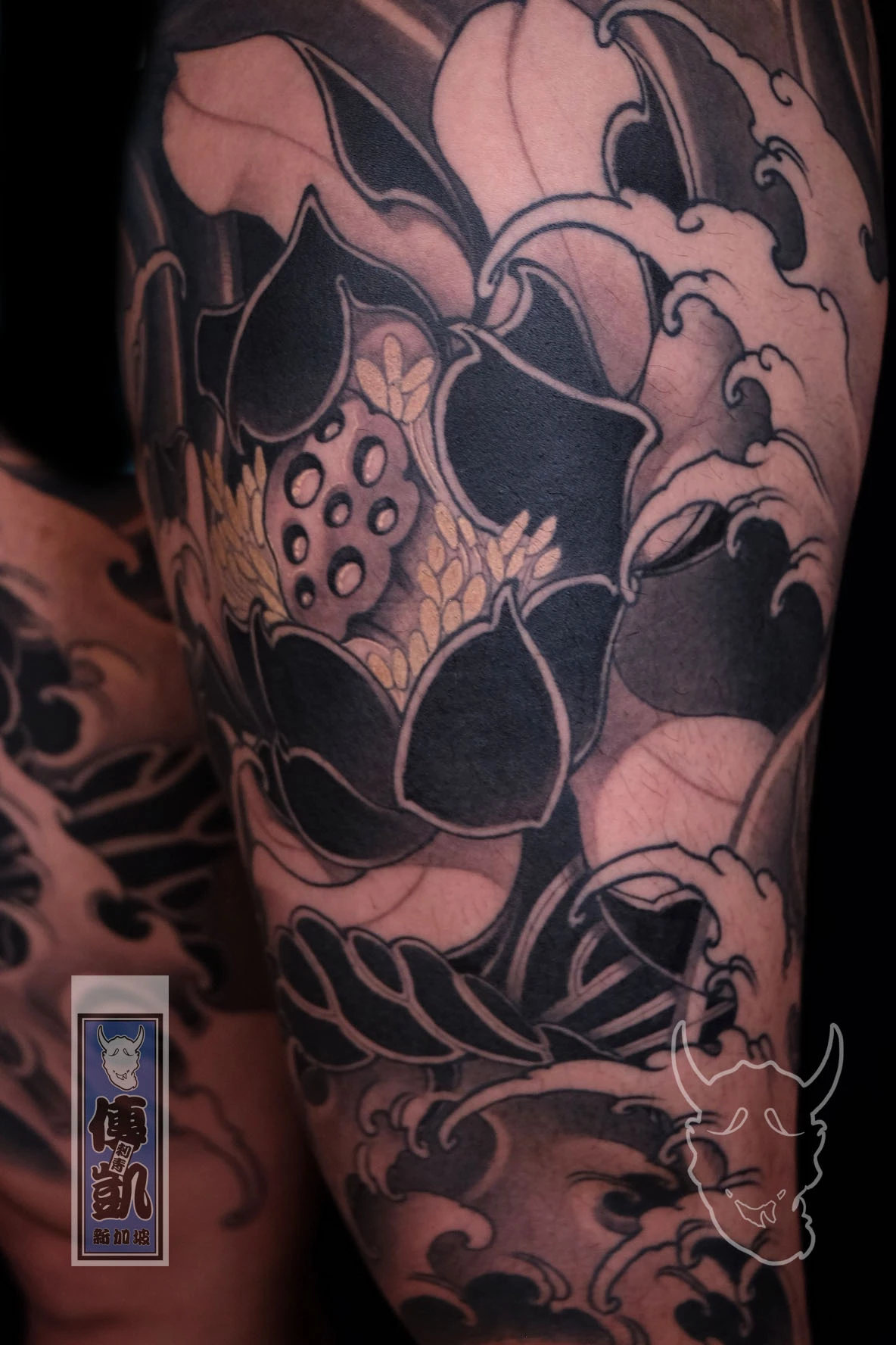 New Traditional Japanese leg tattoo of a black and grey lotus surrounded by flowing waves and clouds, symbolizing purity and balance in modern tattoo art.