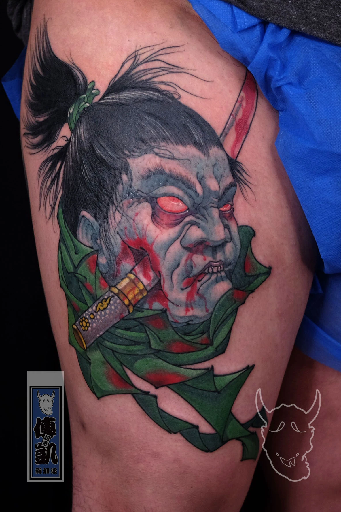 Traditional Japanese Namakubi tattoo of a severed samurai head wrapped in green cloth on the thigh, symbolizing honor and acceptance of death. Artwork by CK Tattoo Singapore.