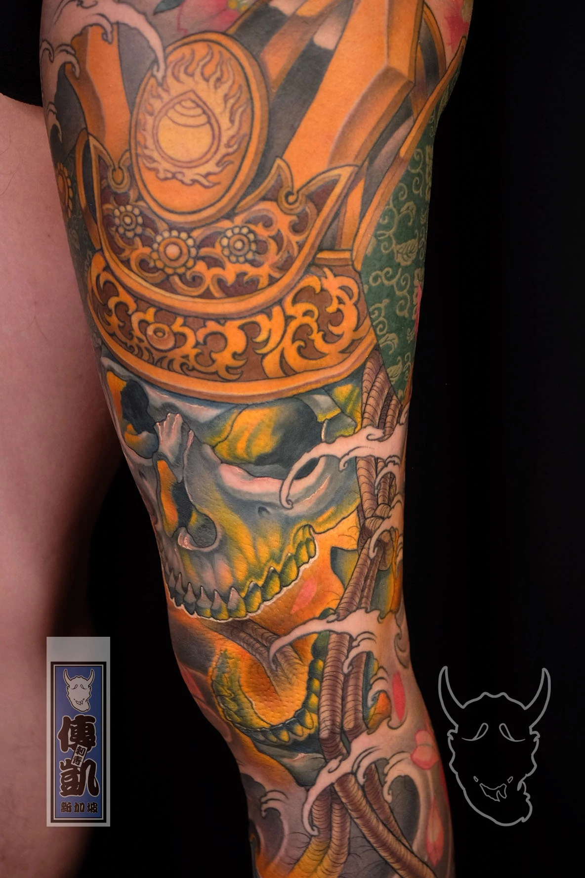 New Traditional Japanese leg tattoo of a samurai skull wearing a golden kabuto helmet, surrounded by waves and florals.