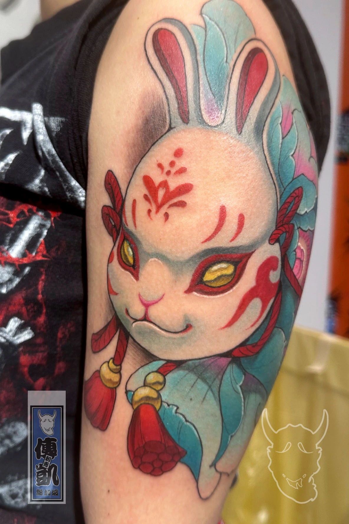 Japanese Usagi rabbit tattoo on upper arm with red markings and teal botan flowers, symbolizing courage and protection. Artwork by CK Tattoo Singapore.