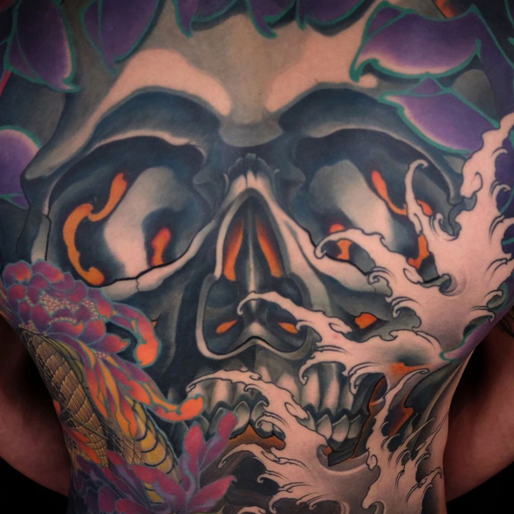 Japanese skull and kiku chrysanthemum back tattoo with glowing eyes serpent and waves by CK Tattoo Singapore