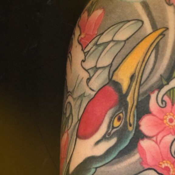 Japanese crane arm sleeve tattoo featuring a crane in flight among blossoms and waves, symbolizing peace, loyalty, and balance in traditional Irezumi style.