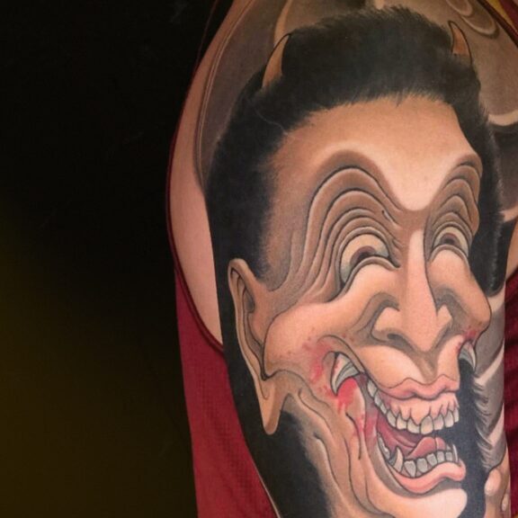 Japanese Hannya mask arm tattoo with surreal distorted facial features, symbolizing emotional duality and inner transformation in contemporary Irezumi art.