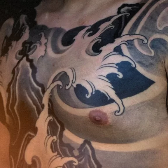 New Traditional Japanese full front tattoo featuring black and grey wave patterns flowing across the chest and torso, symbolizing strength and movement in modern Japanese tattoo art style.