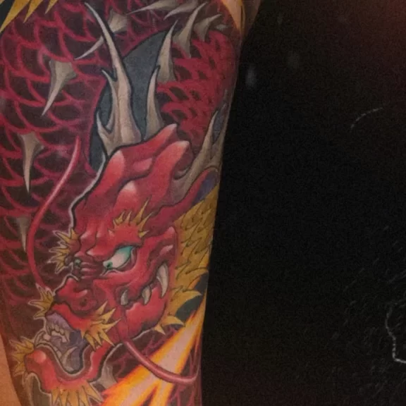New Traditional Japanese red dragon tattoo on the leg, featuring bold red scales, dynamic lightning, and flowing wind bars — a modern take on traditional Japanese tattoo art.