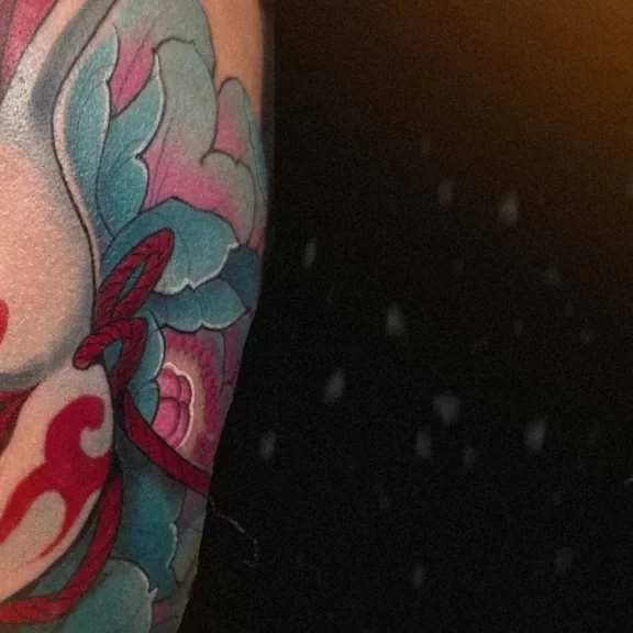 Japanese Usagi rabbit tattoo on upper arm with red markings and teal botan flowers, symbolizing courage and protection. Artwork by CK Tattoo Singapore.